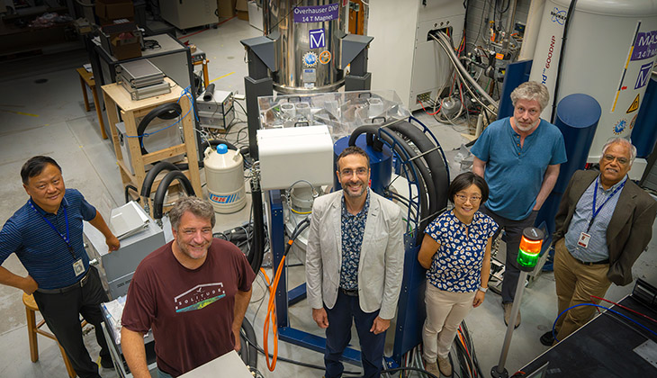 A group of six people standing in a science lab looking up at a camera.