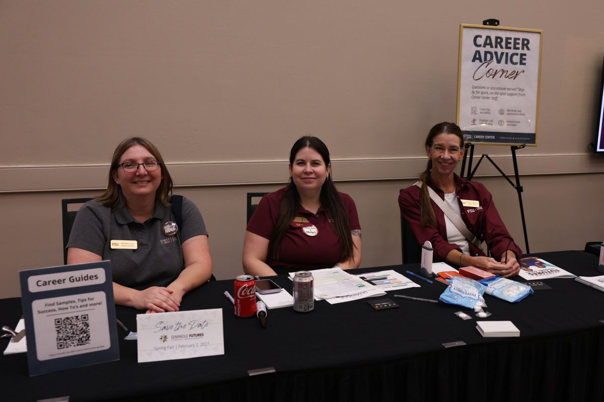 Three FSU Career Center staff members smile while seated behind a table labeled "Career Advice Corner" with resource signages and guides.