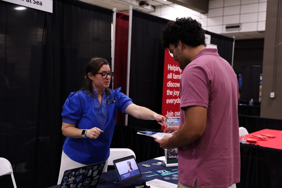 A representative in a blue top points to informational brochures while speaking with a student at a Semester at Sea booth.