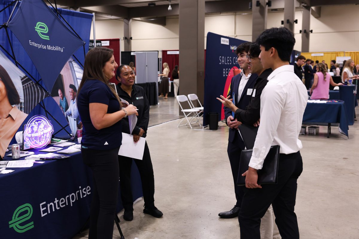 A group of three male students speak with two representatives at an Enterprise Mobility career booth.